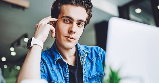 Young man in front of a laptop staring at the viewer